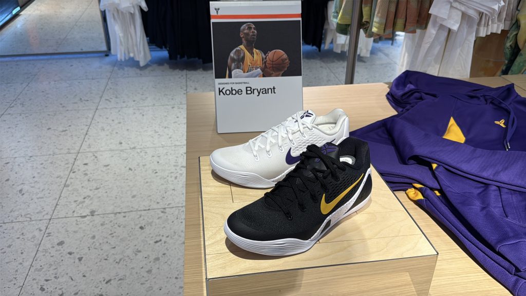 In-store Kobe Bryant display with a placard, a black and gold sneaker, a white and purple sneaker, and Lakers apparel