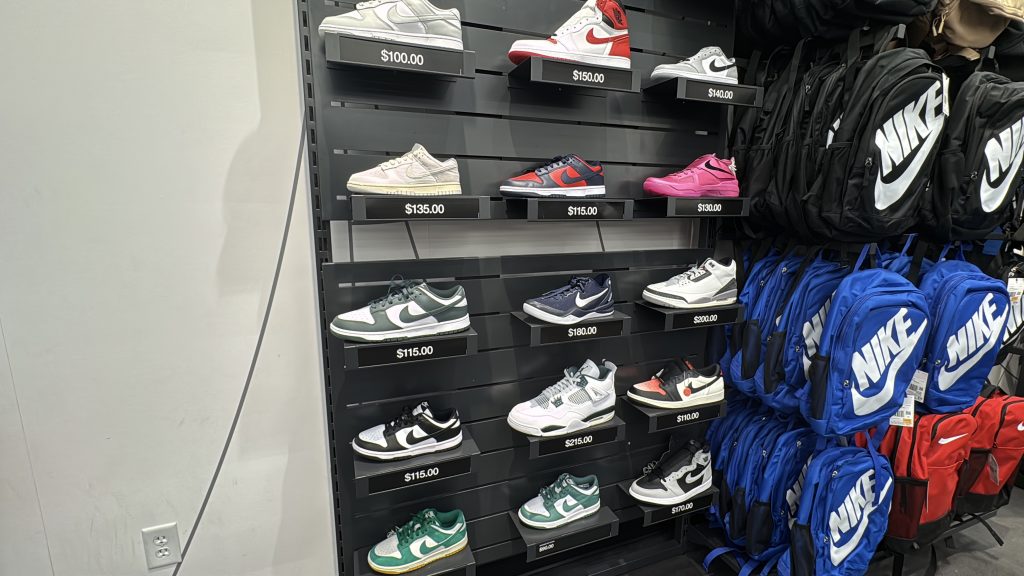 A wall display of Nike sneakers in-store beside a rack of Nike drawstring bags